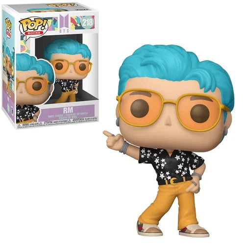 Funko Pop! Rocks BTS Dynamite RM vinyl figure (#218) featuring blue hair, orange sunglasses, black star shirt, and yellow pants with figure box in background.