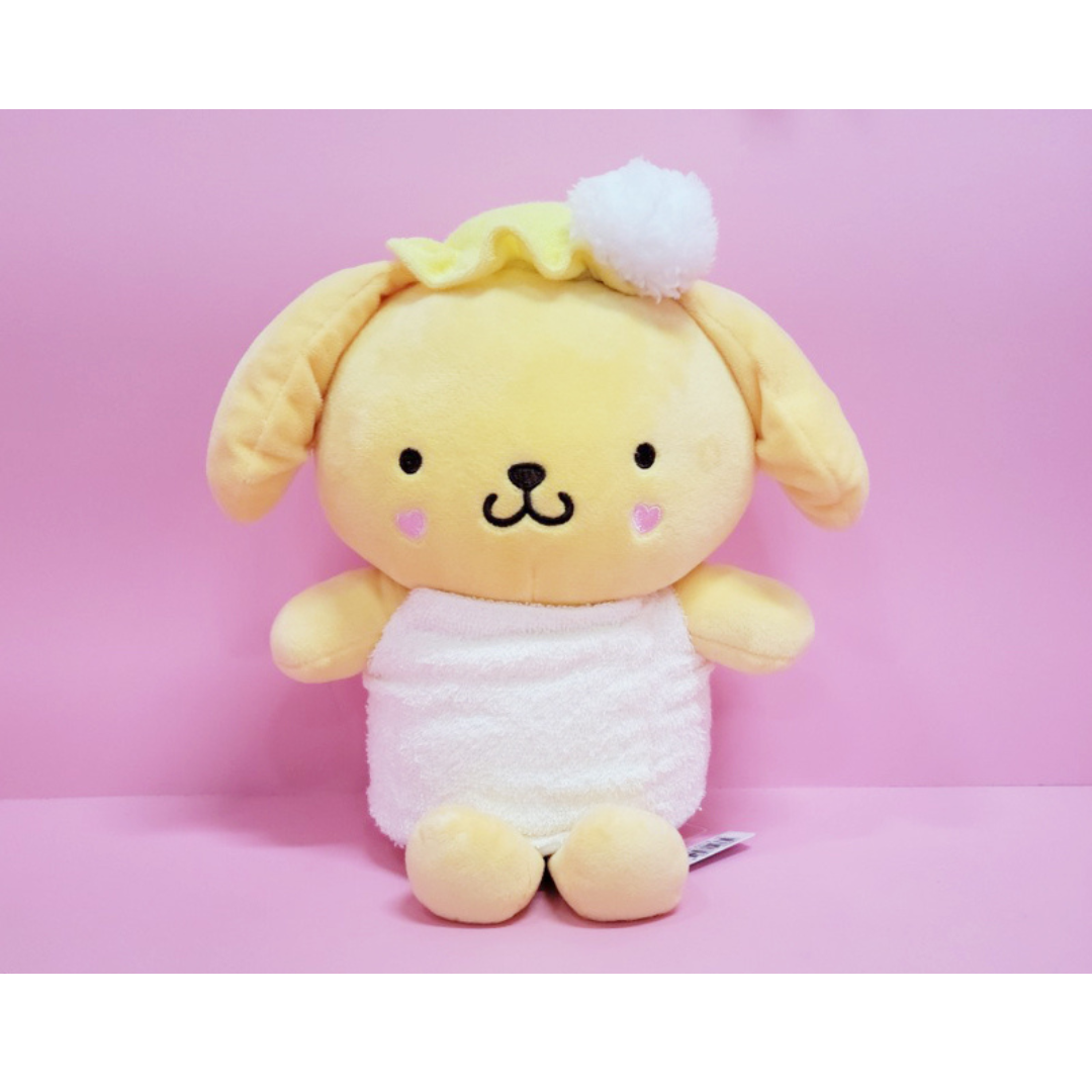 Pompompurin plush toy wearing a fluffy white towel and yellow ruffled shower cap with a white pom-pom, seated against a pastel pink background.