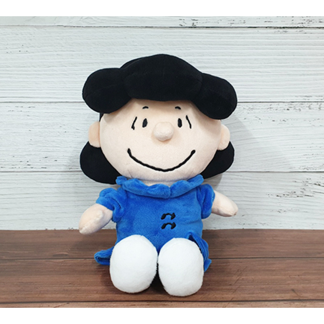Lucy van Pelt plush doll from Peanuts, wearing a blue dress and white shoes, sitting against a wood-textured background — ideal collectible gift for Peanuts fans and kids.