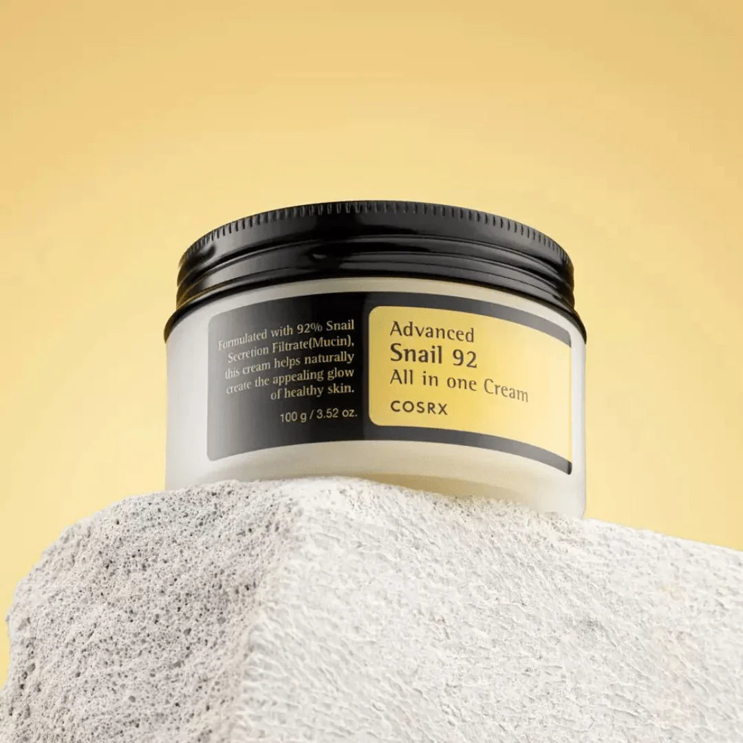 Cosrx Advanced Snail 92 All-in-One Cream jar on a textured surface with a yellow gradient background