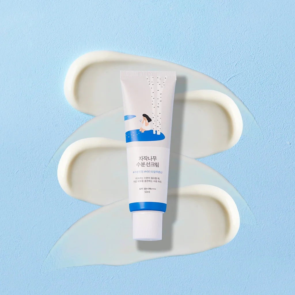 A white skincare tube with blue accents and Korean text, placed upright on a light blue background with cream-colored cream swirls behind it.
